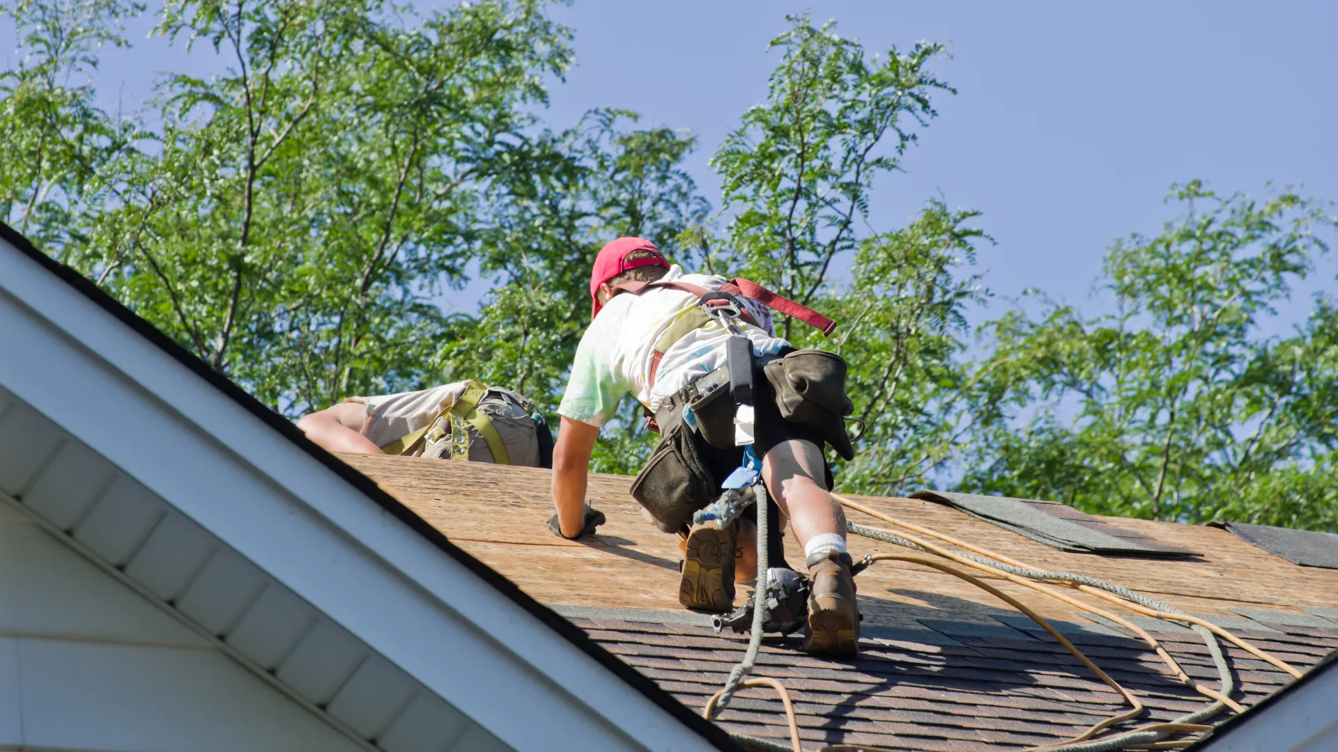 A roofer in a red cap crawls across exposed roof decking