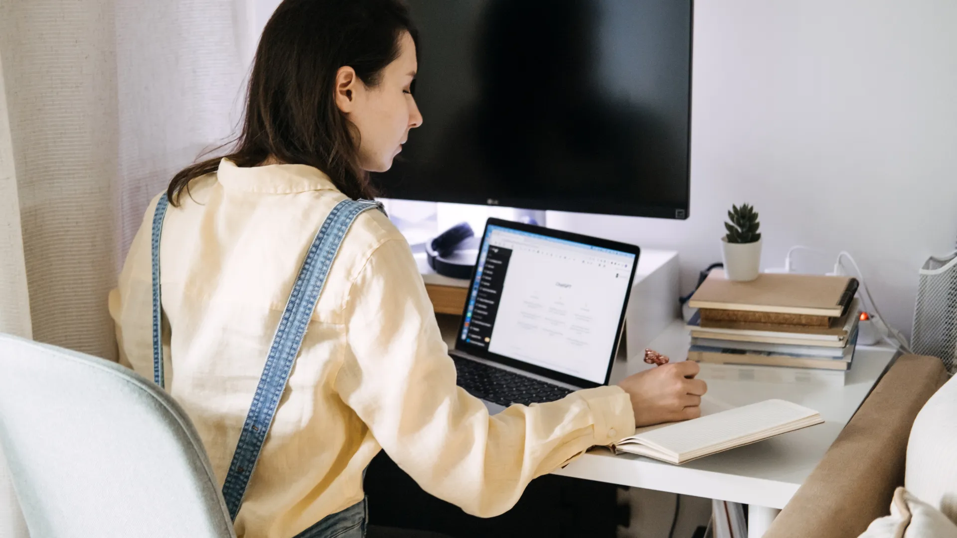 Woman taking notes at her desk beside an open laptop