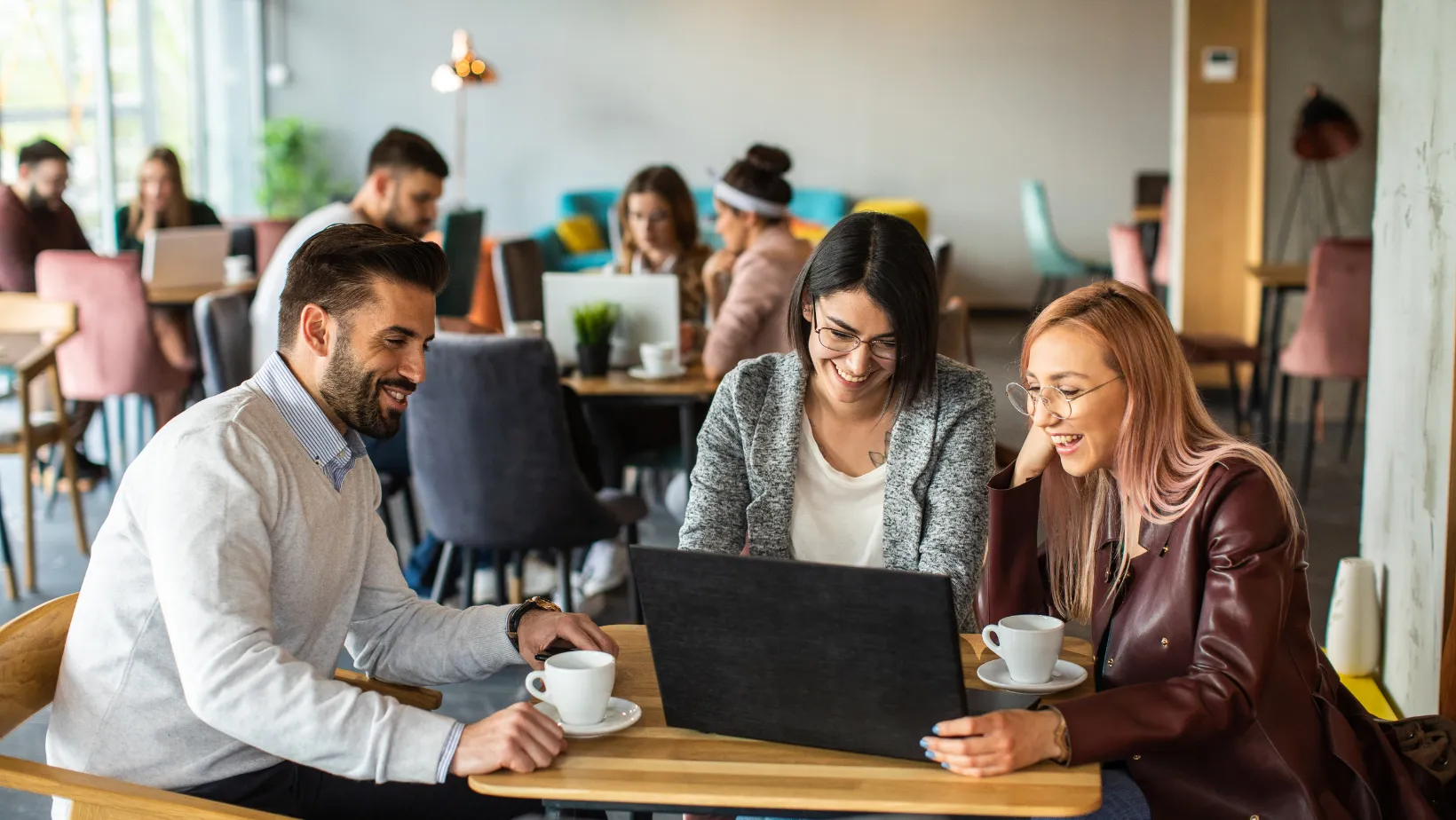 Three colleagues smiling at a laptop in a busy Toronto cafe