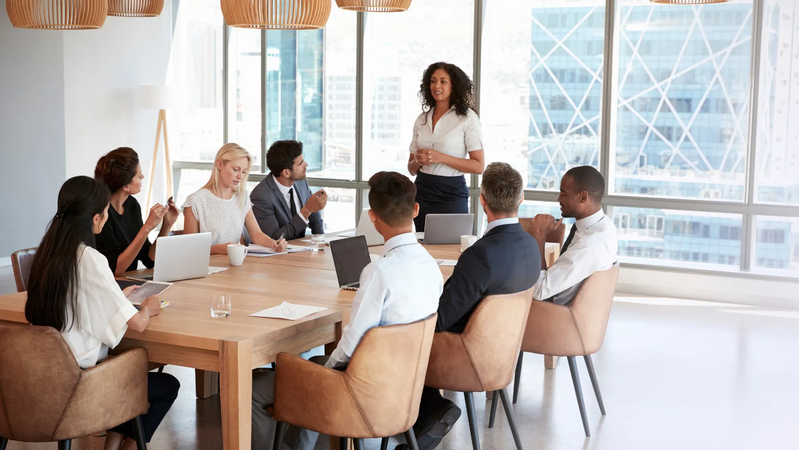 Business team meeting around a boardroom table while a woman presents