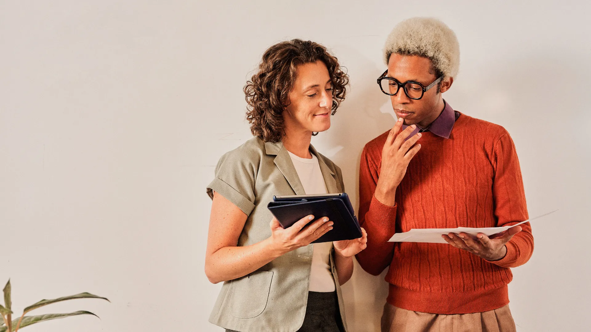 Two colleagues reviewing a tablet and a printed page together