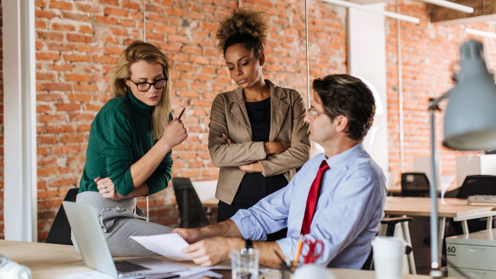 Three colleagues reviewing a document at a desk in a brick-walled office