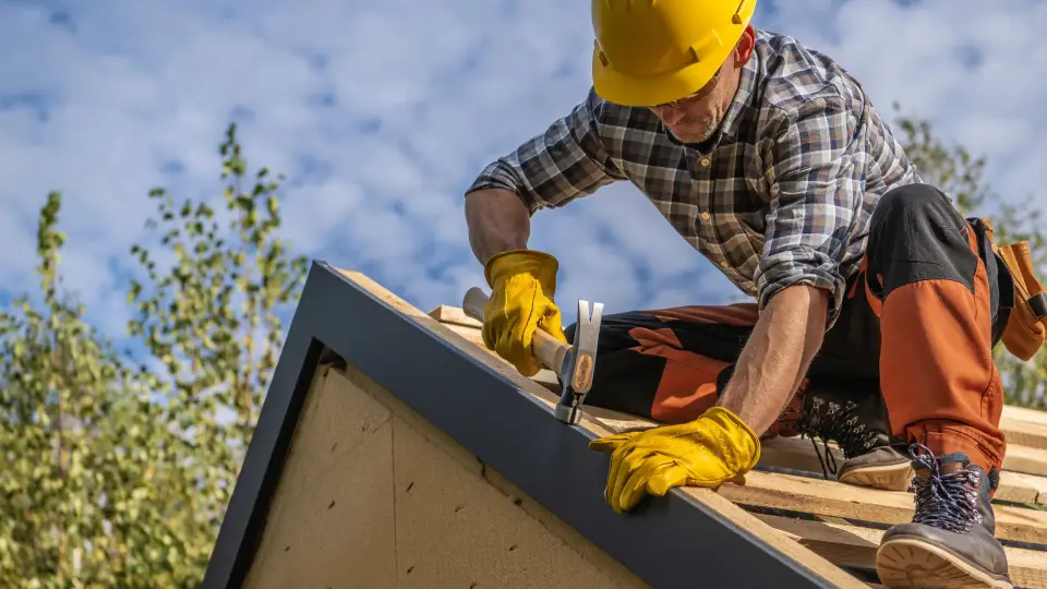 Roofing contractor in a hard hat nailing down roof sheathing