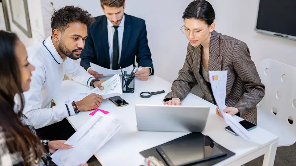 Marketing team reviewing campaign reports around a laptop