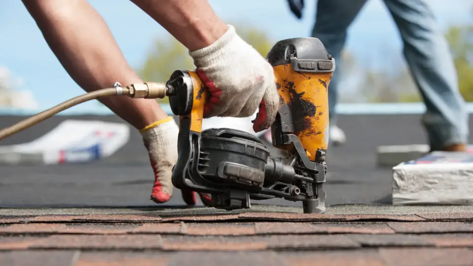 Roofer using a nail gun on asphalt shingles