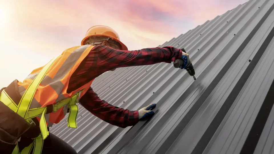 Roofer fastening a metal roof panel with a cordless drill