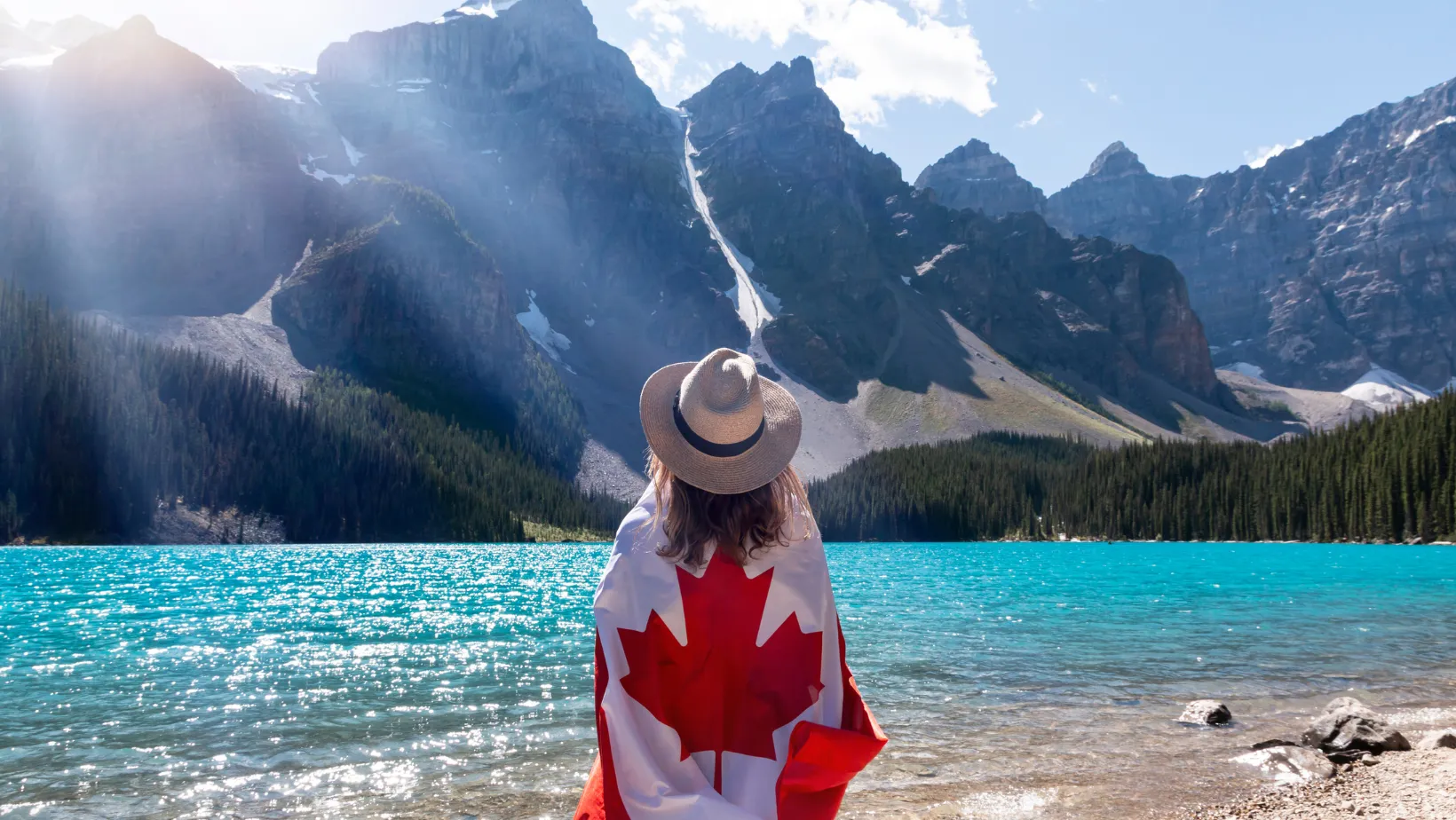 Woman wrapped in a Canadian flag looking out at Moraine Lake and the Rocky Mountains