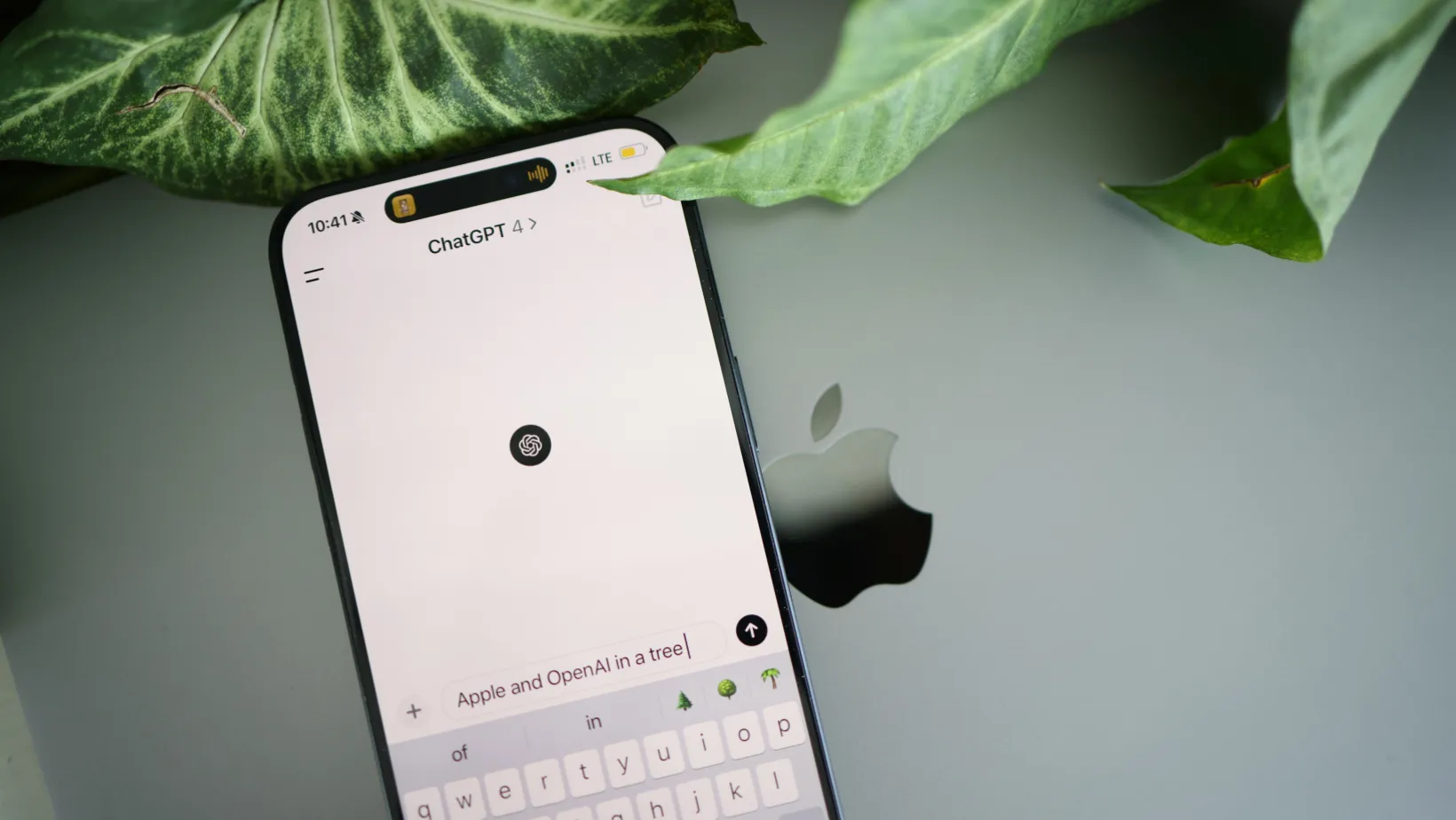 Phone with the ChatGPT app open on a laptop lid beside green leaves