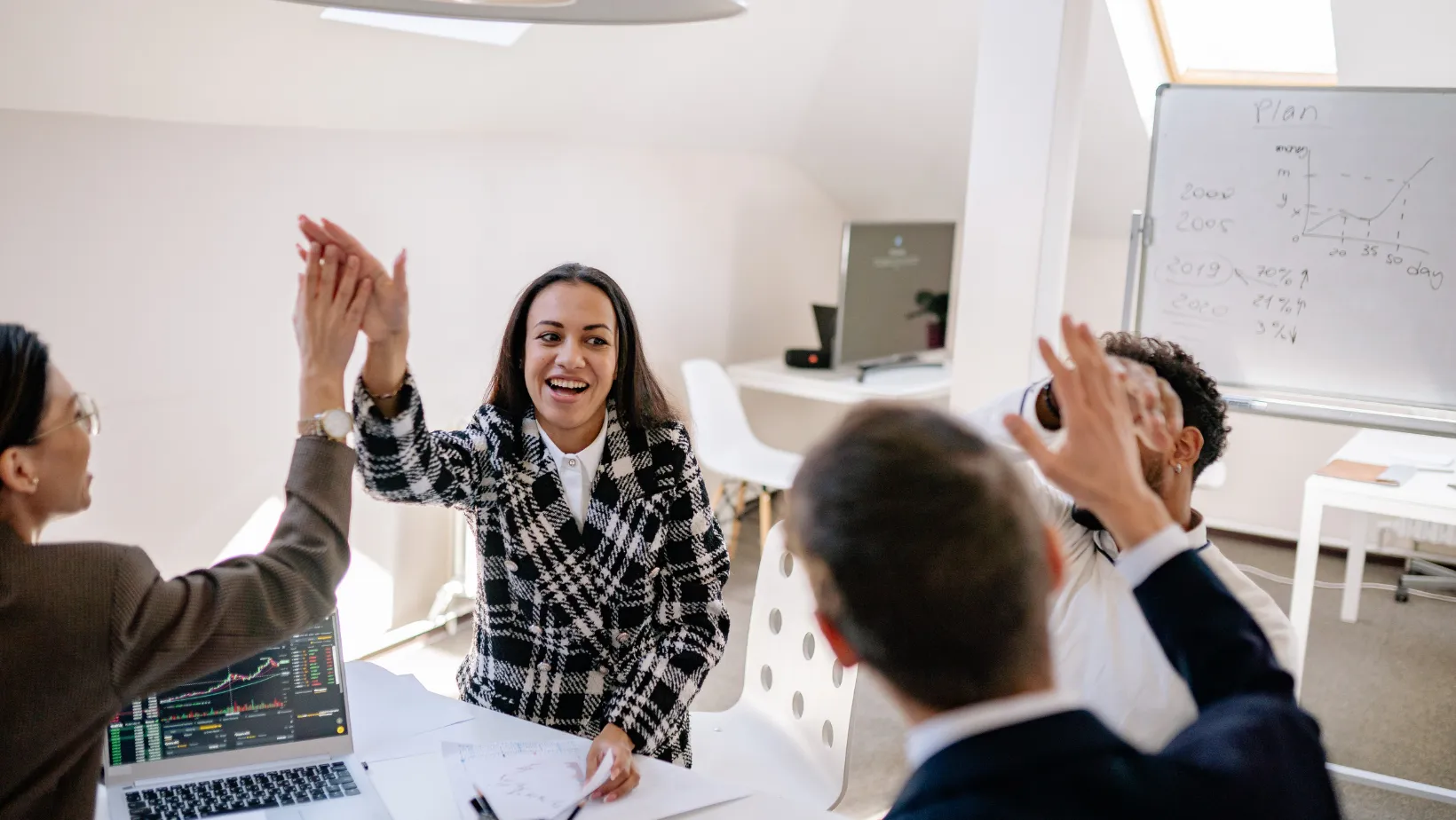 Marketing team sharing high fives at a table next to a growth plan on a whiteboard