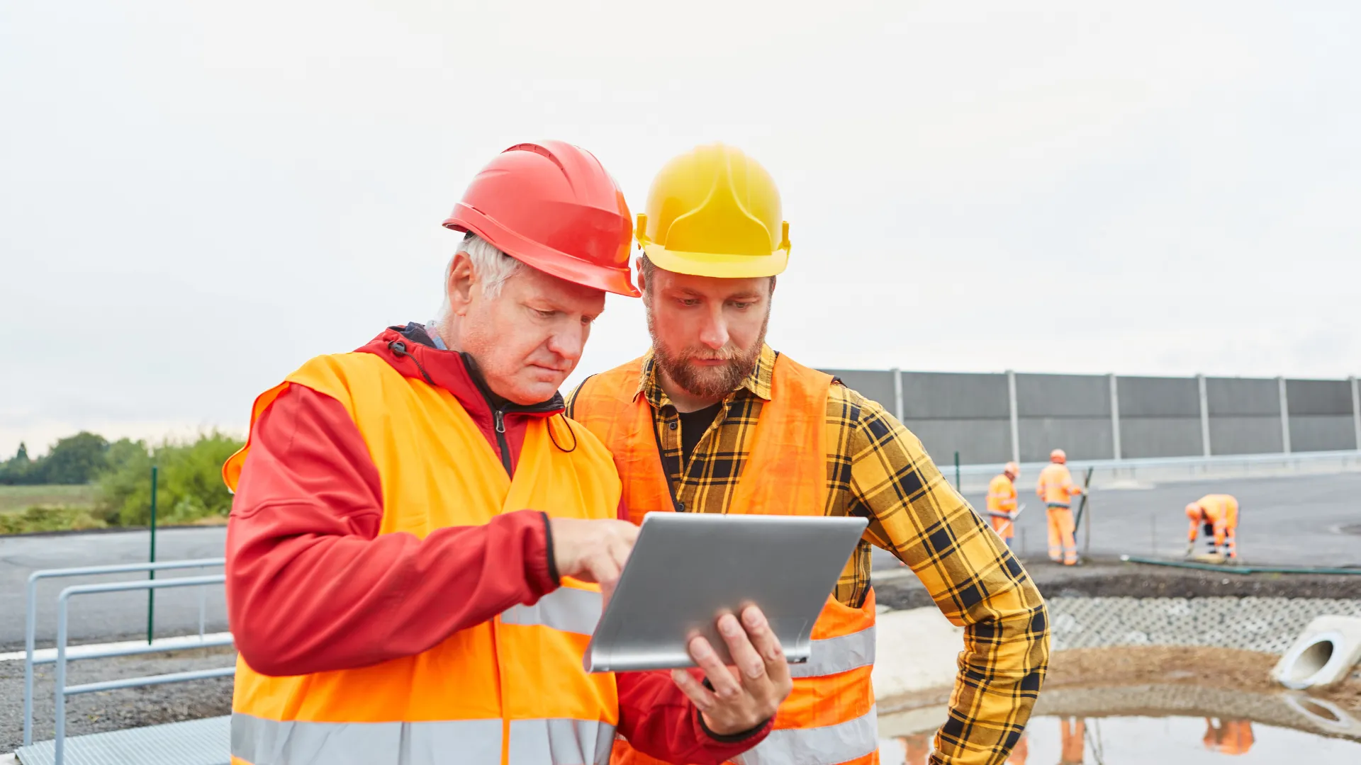 Two site leads check a tablet while a crew works behind them