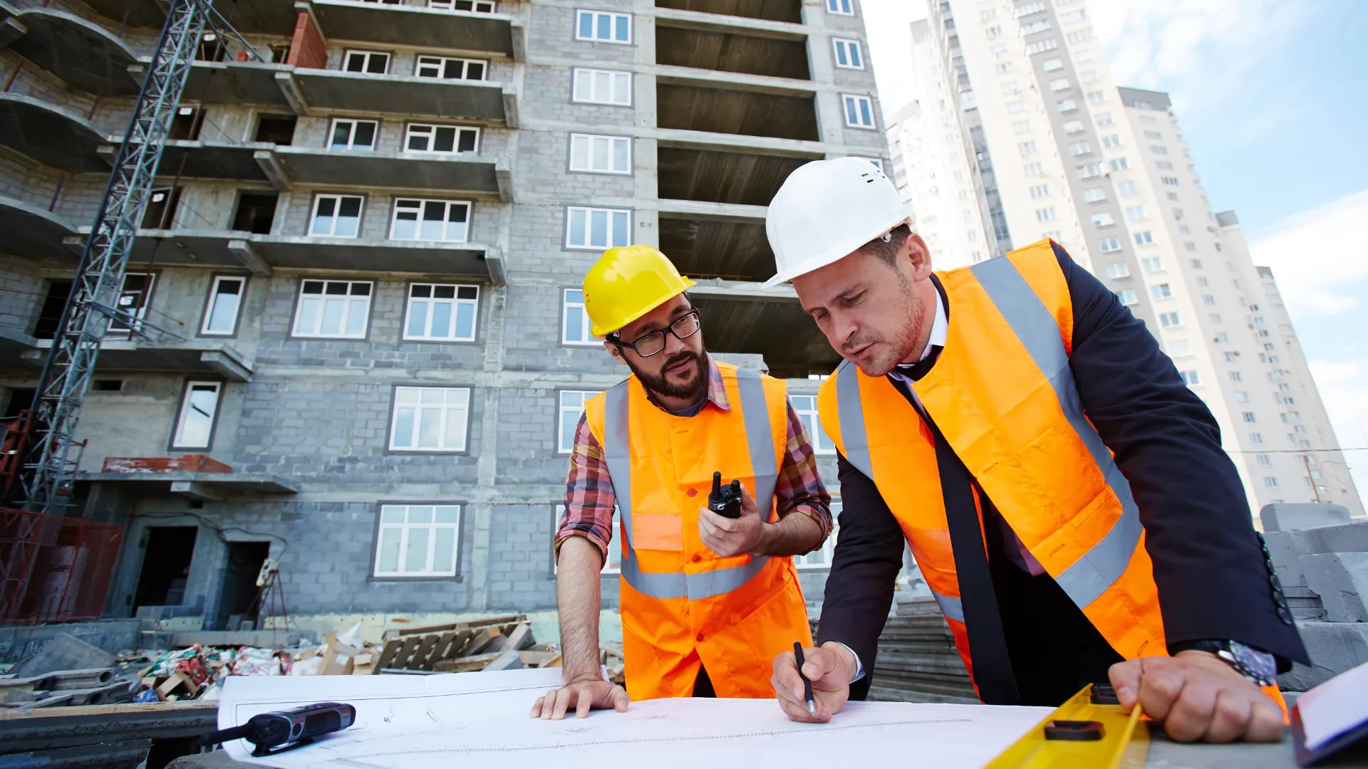 Two contractors review drawings in front of a concrete building under construction