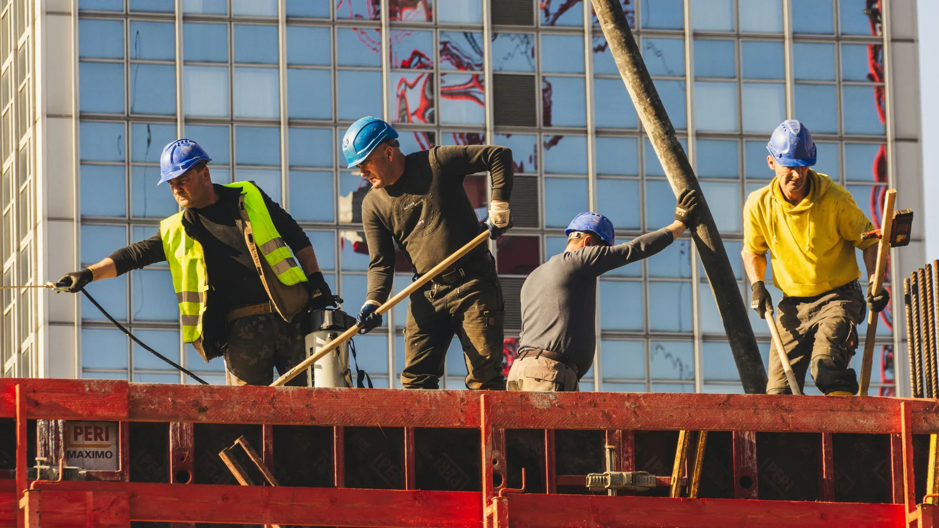 A crew sets formwork on a platform in front of a glass building