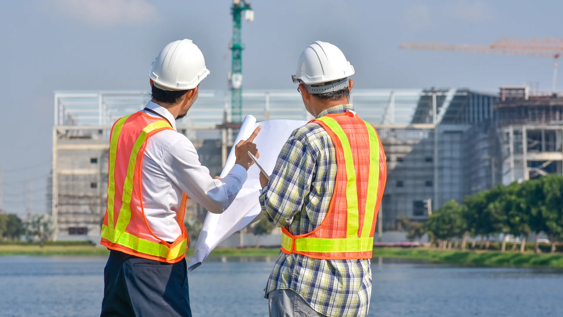 Two contractors review drawings with a commercial job site behind them