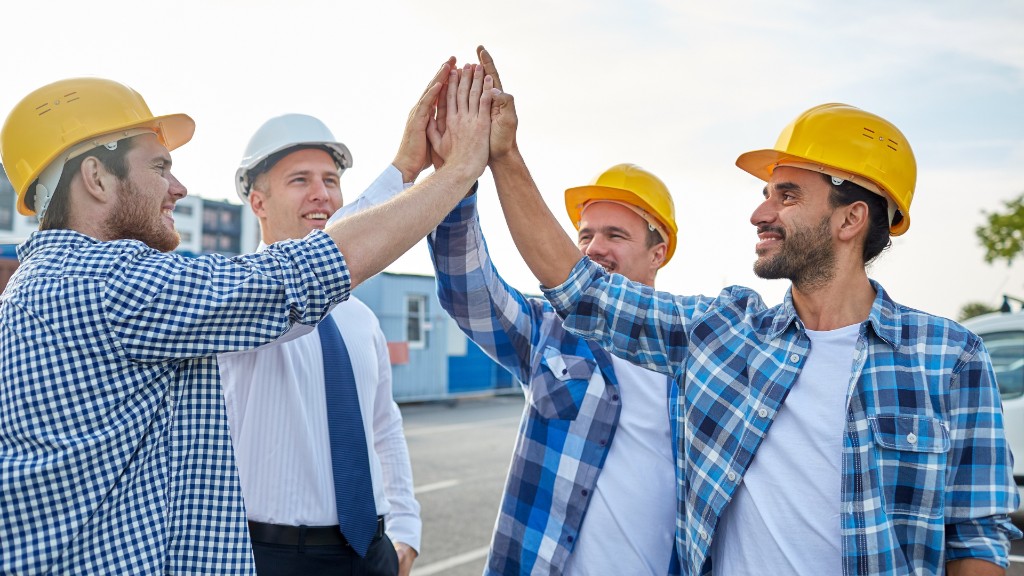 Four contractors in hard hats high-five outside a job site