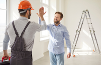 A contractor in an orange hard hat high-fives a colleague beside a ladder