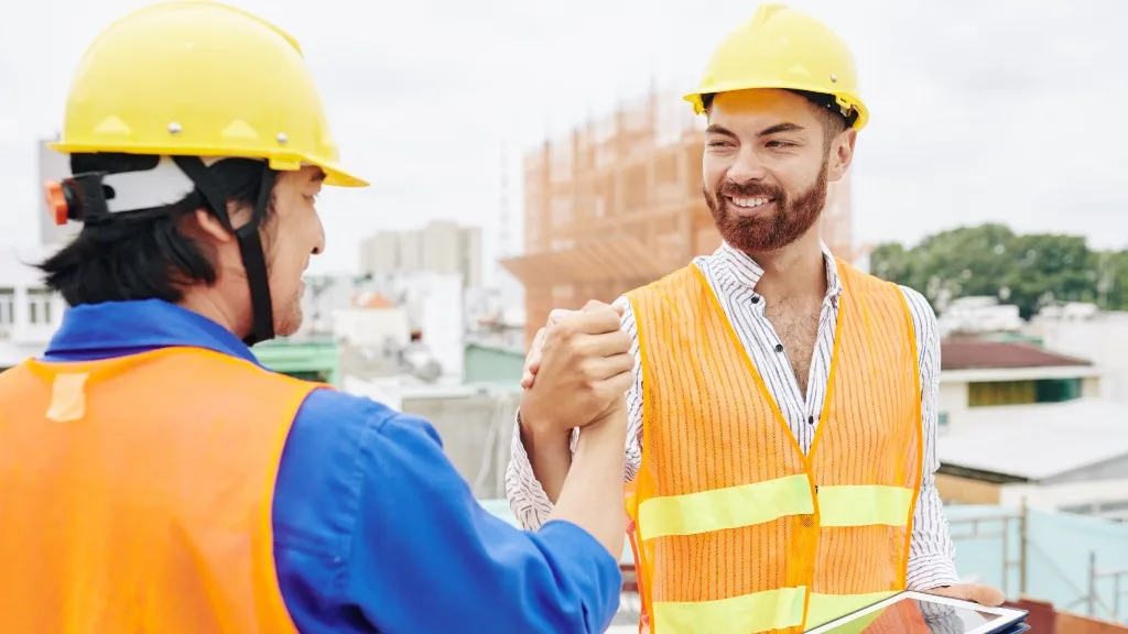 Two contractors in hard hats fist-bump on a rooftop job site