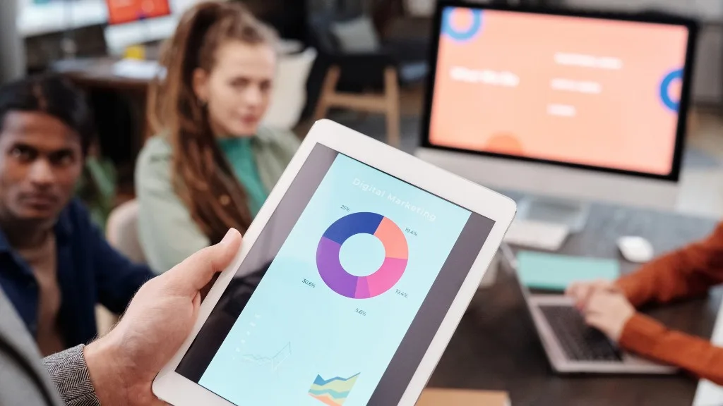 A tablet shows a digital marketing chart during a team meeting
