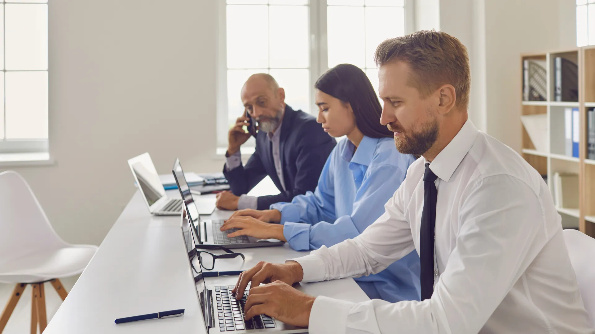 A marketing team works on laptops in a bright office, with one colleague on a phone call