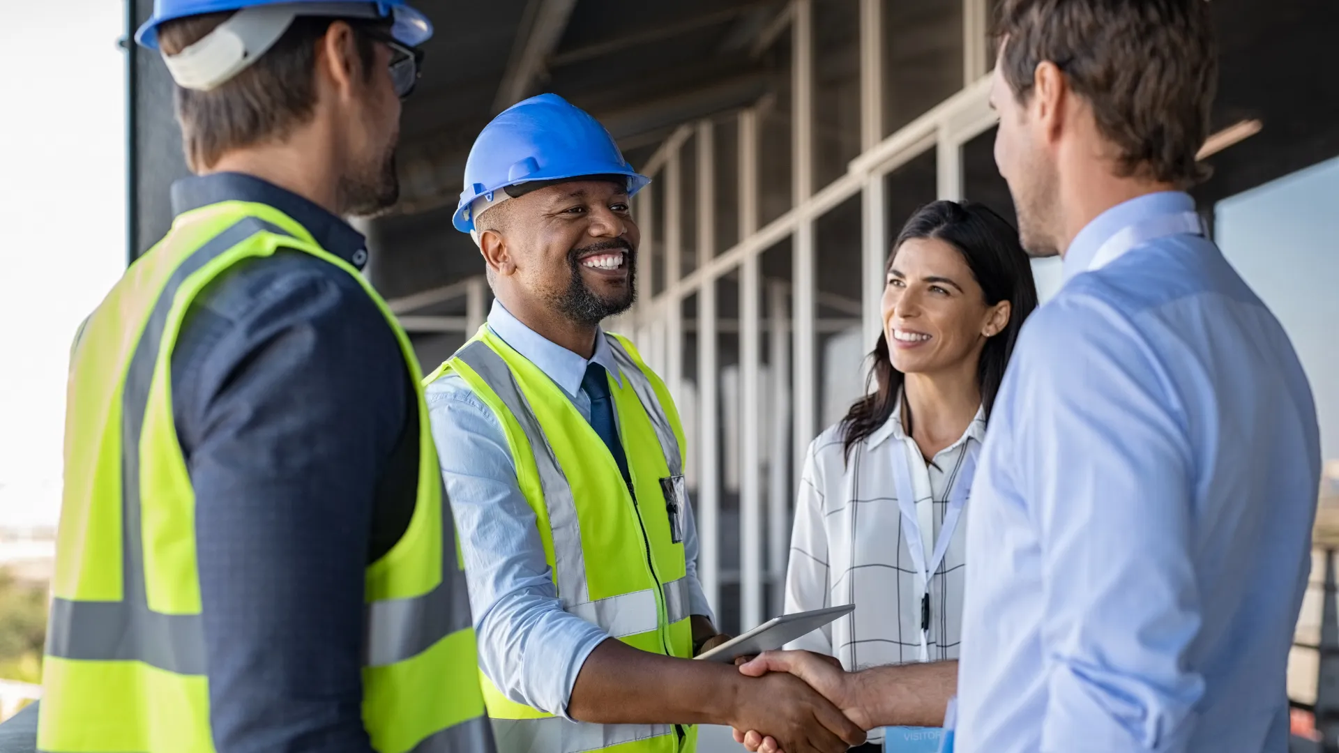 A site lead in a hard hat shakes hands with a client outside a building