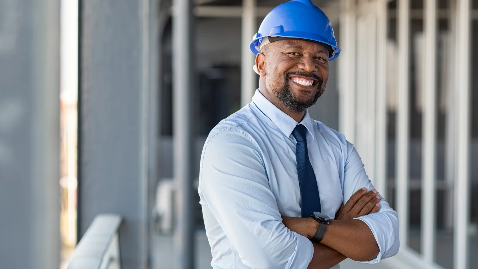 Smiling contractor in a blue hard hat with his arms crossed on a job site