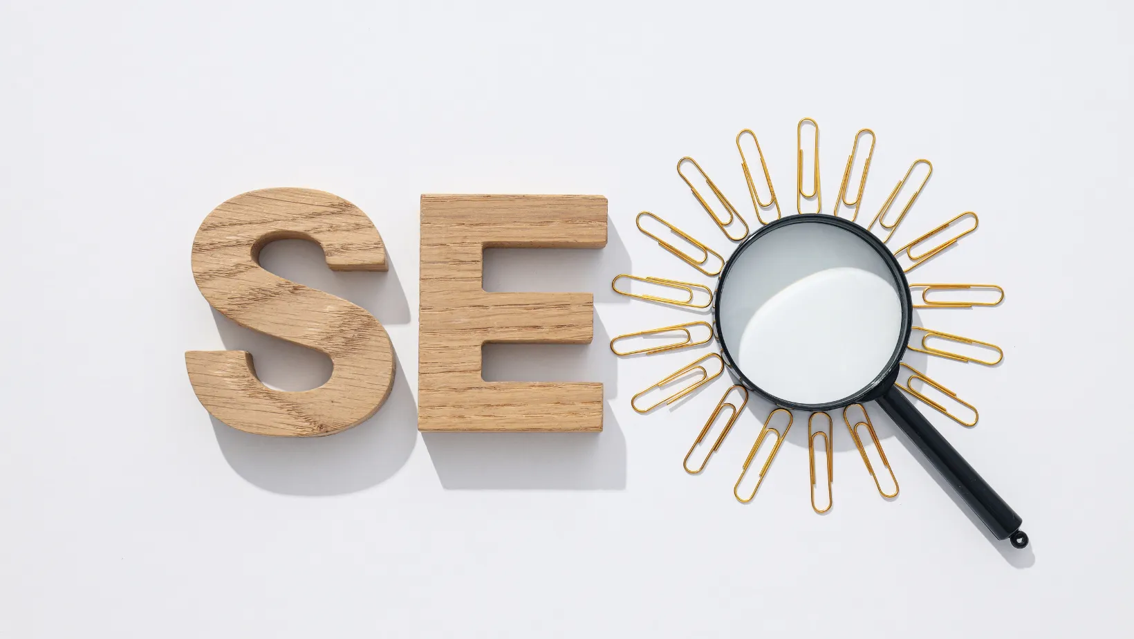 Wooden letters S and E next to a magnifying glass ringed with paper clips, spelling SEO