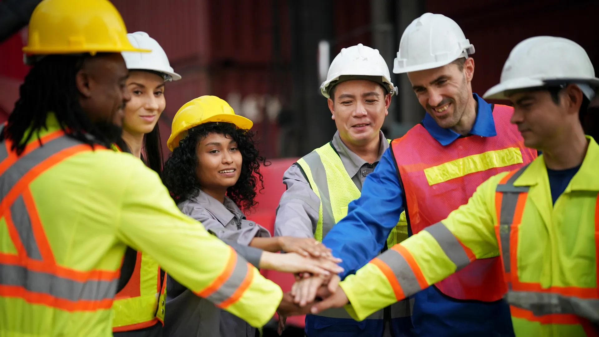 Contractors in hard hats and safety vests stack their hands together