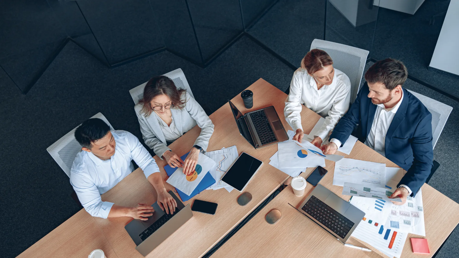 Four colleagues review charts and laptops around a conference table