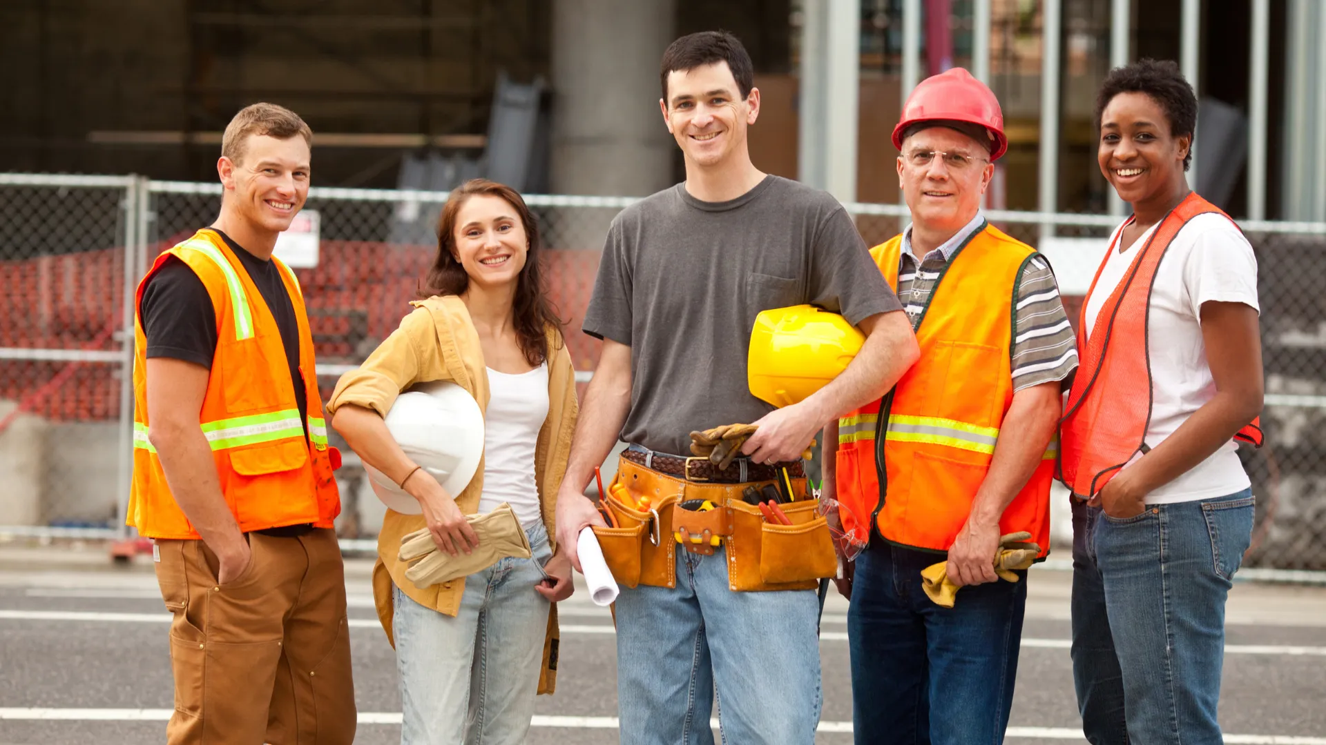 Five contractors in safety vests smile at a job site