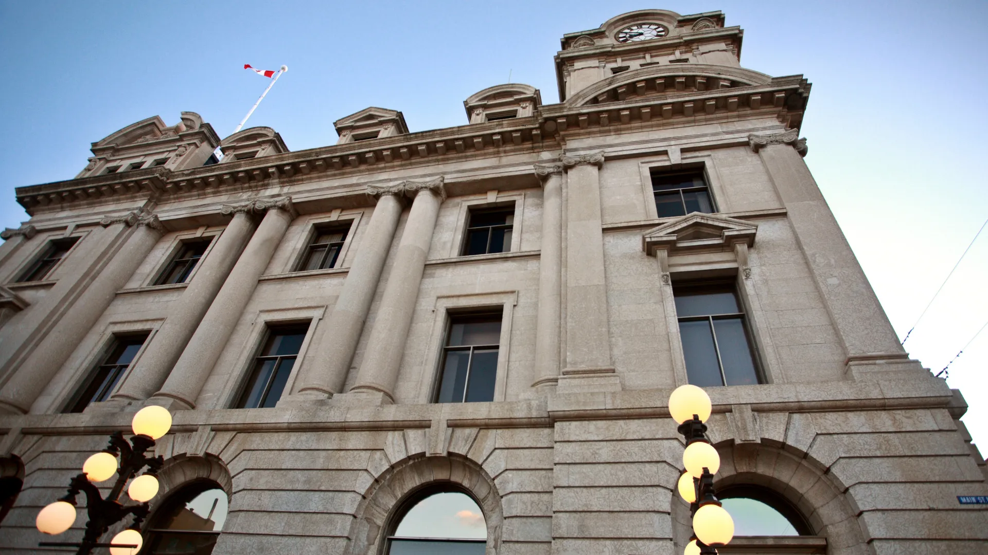 A stone civic building with a clock tower and a Canadian flag