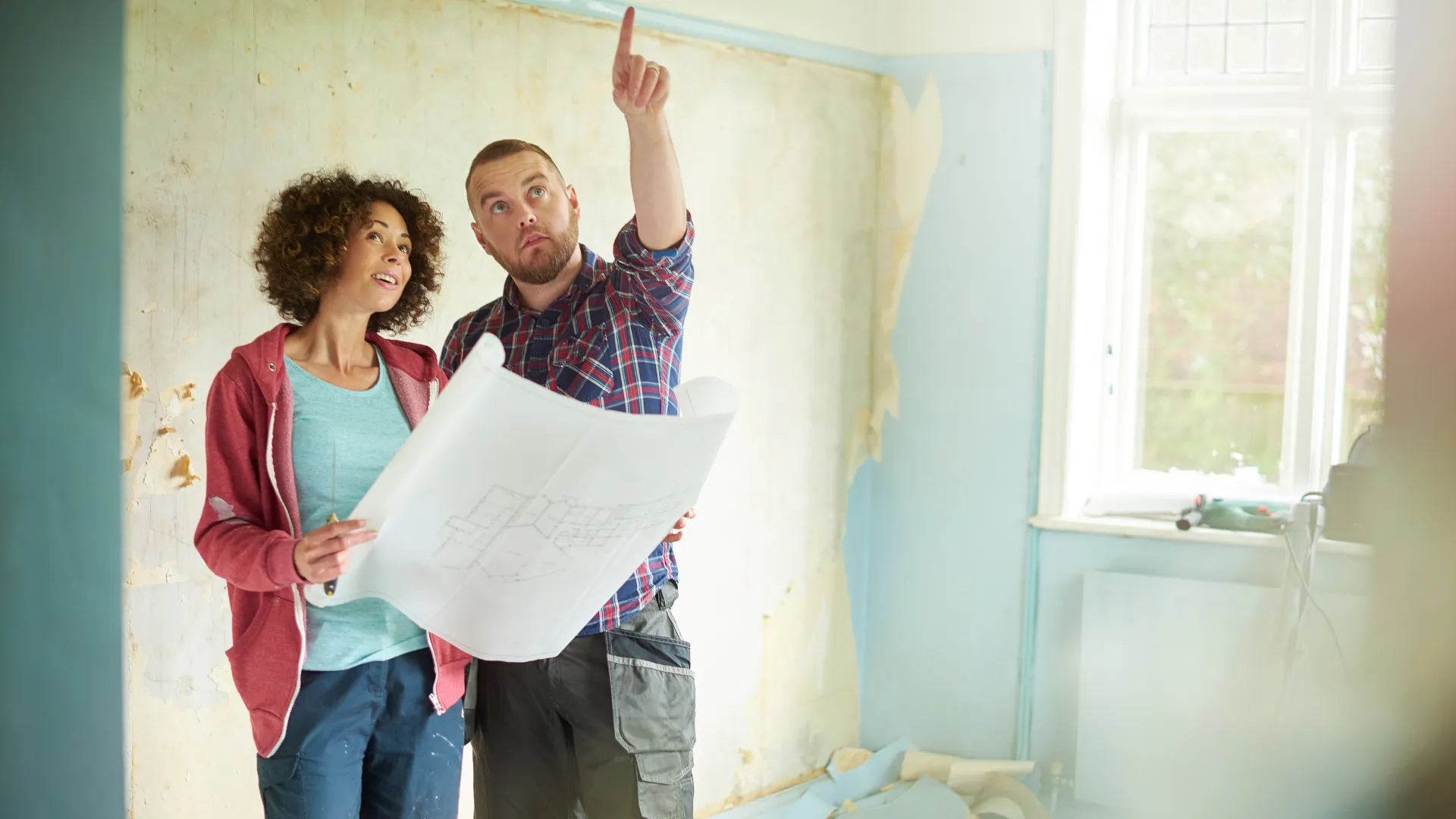 A contractor and a homeowner look over plans in a room being renovated