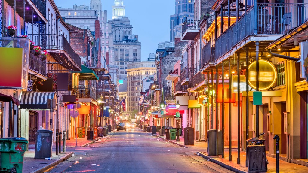 French Quarter street in New Orleans at dusk, lined with balconies and neon signs