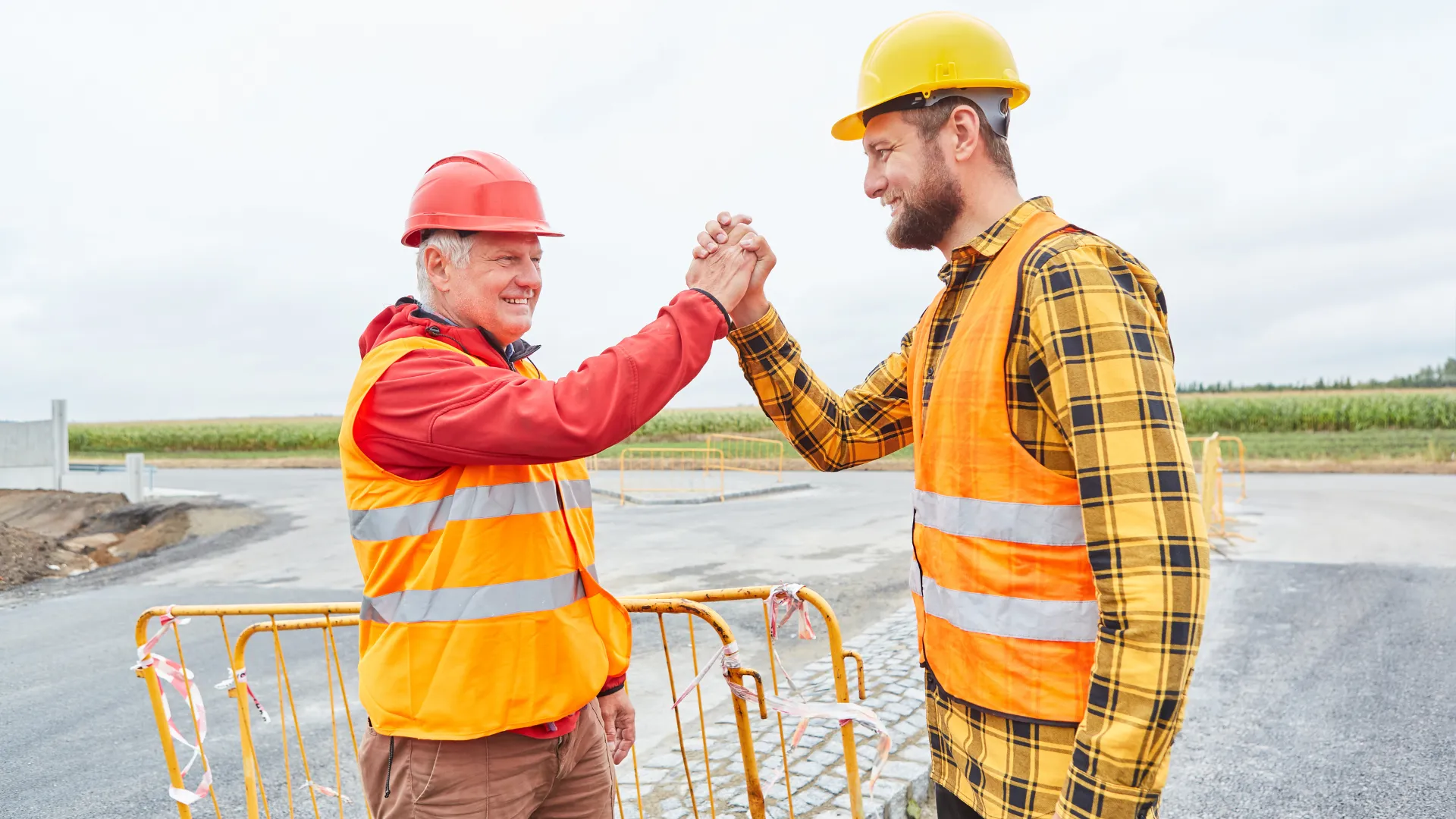 Two site workers in hard hats and safety vests greet each other at a paved job site