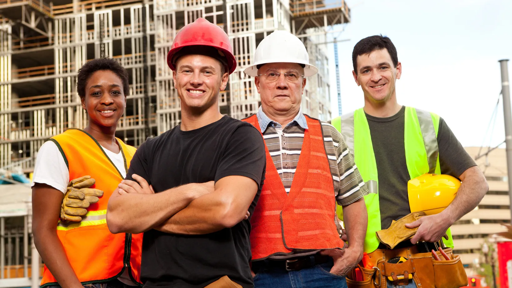 Four contractors in safety vests standing in front of a building under construction