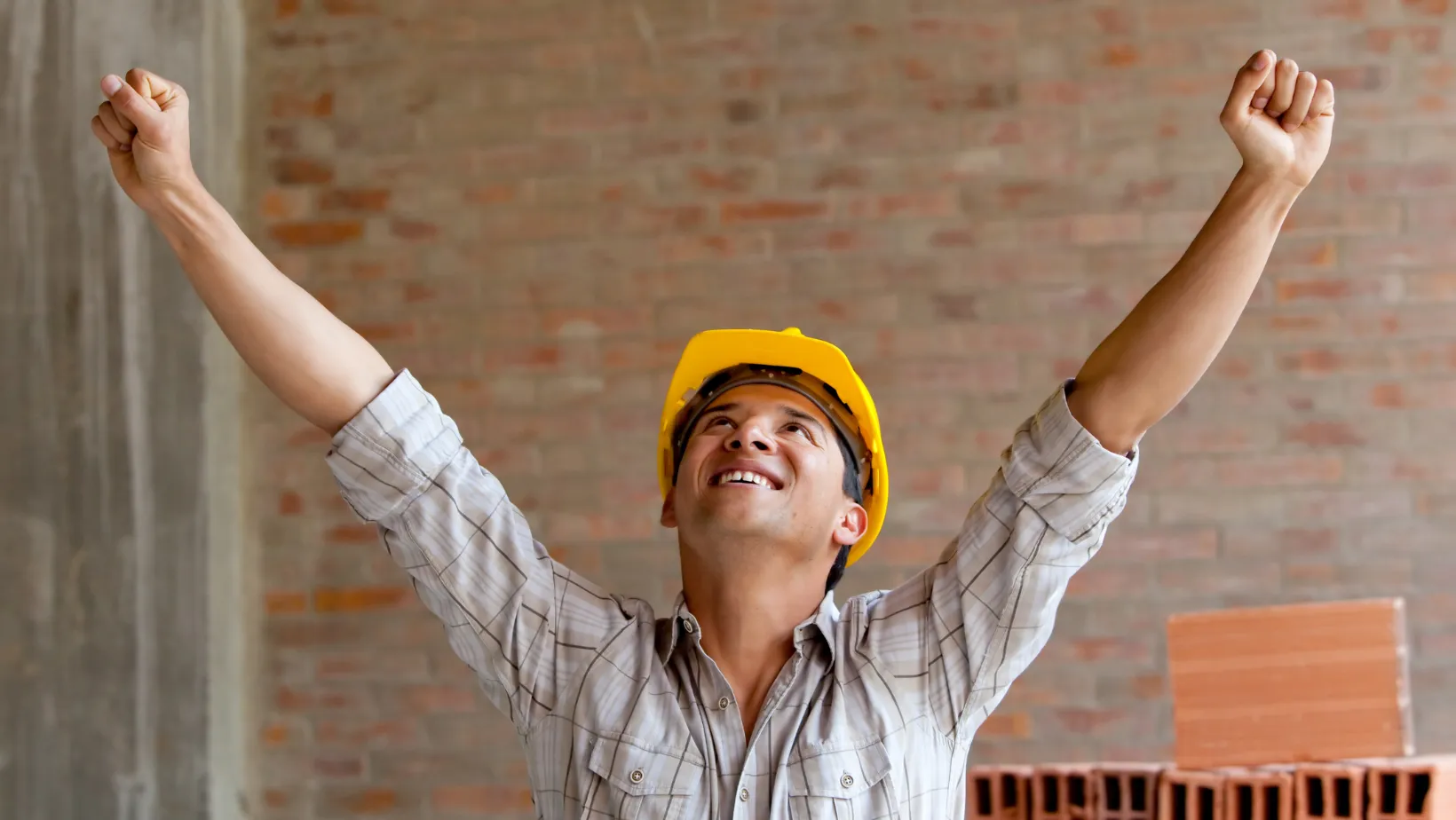 Construction worker in a yellow hard hat raising both arms