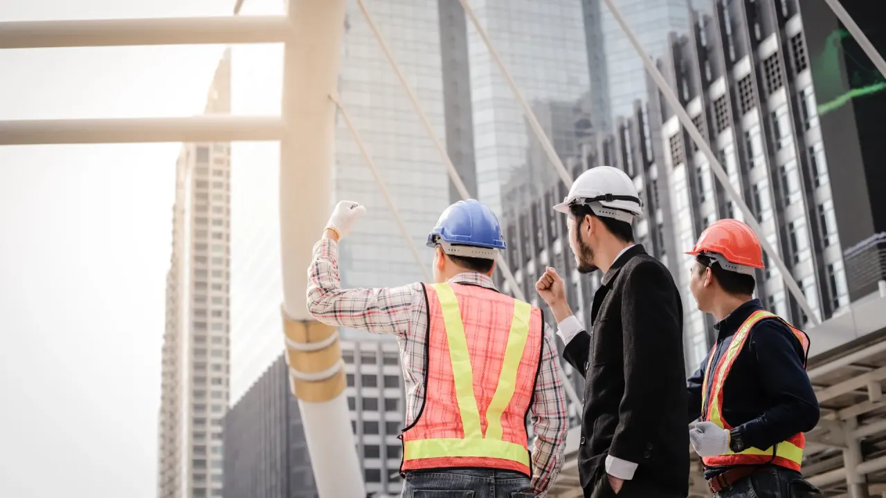 Three construction professionals in safety gear looking toward a modern city skyline from a job site
