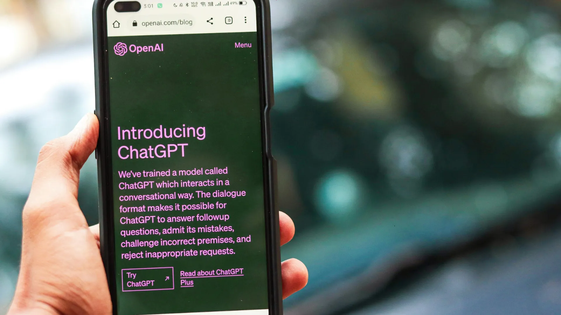 Hand holding a phone showing the OpenAI Introducing ChatGPT page