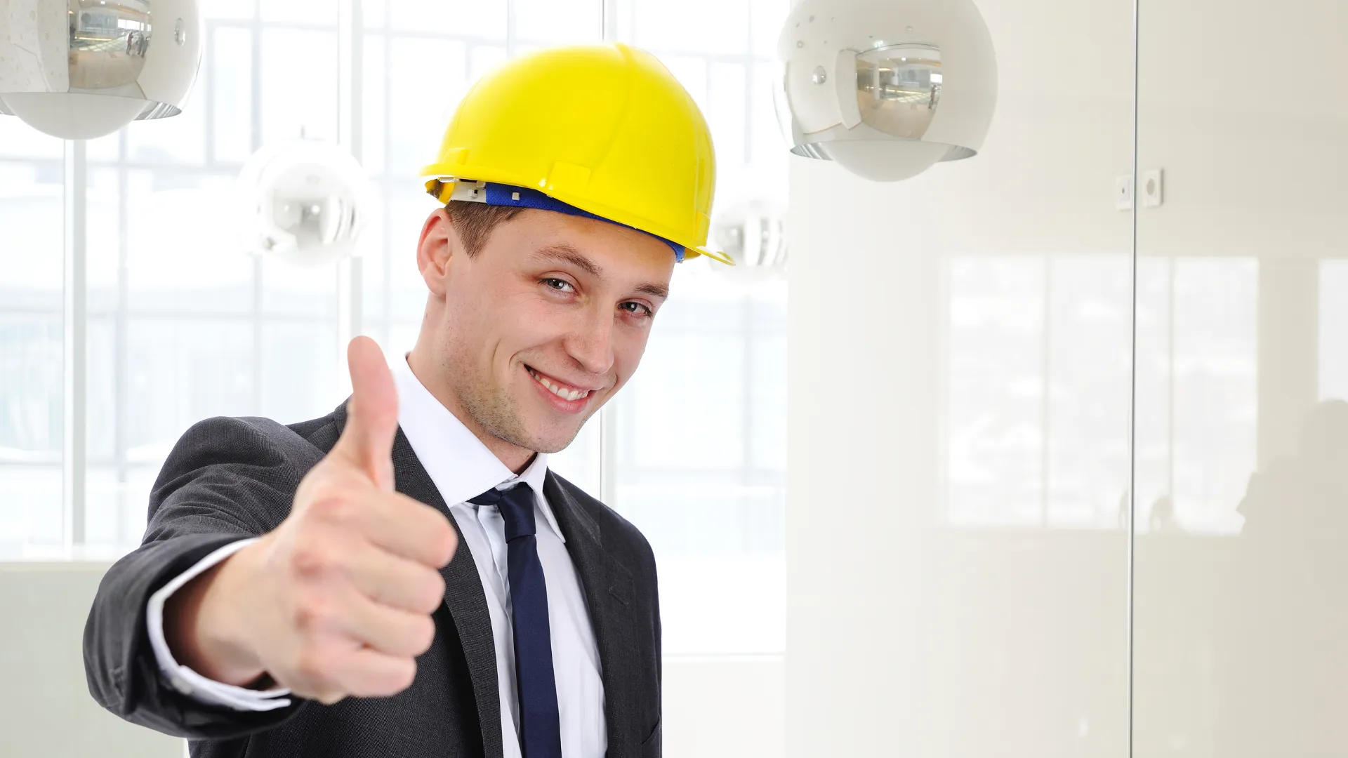 Smiling man in a yellow hard hat and suit giving a thumbs up