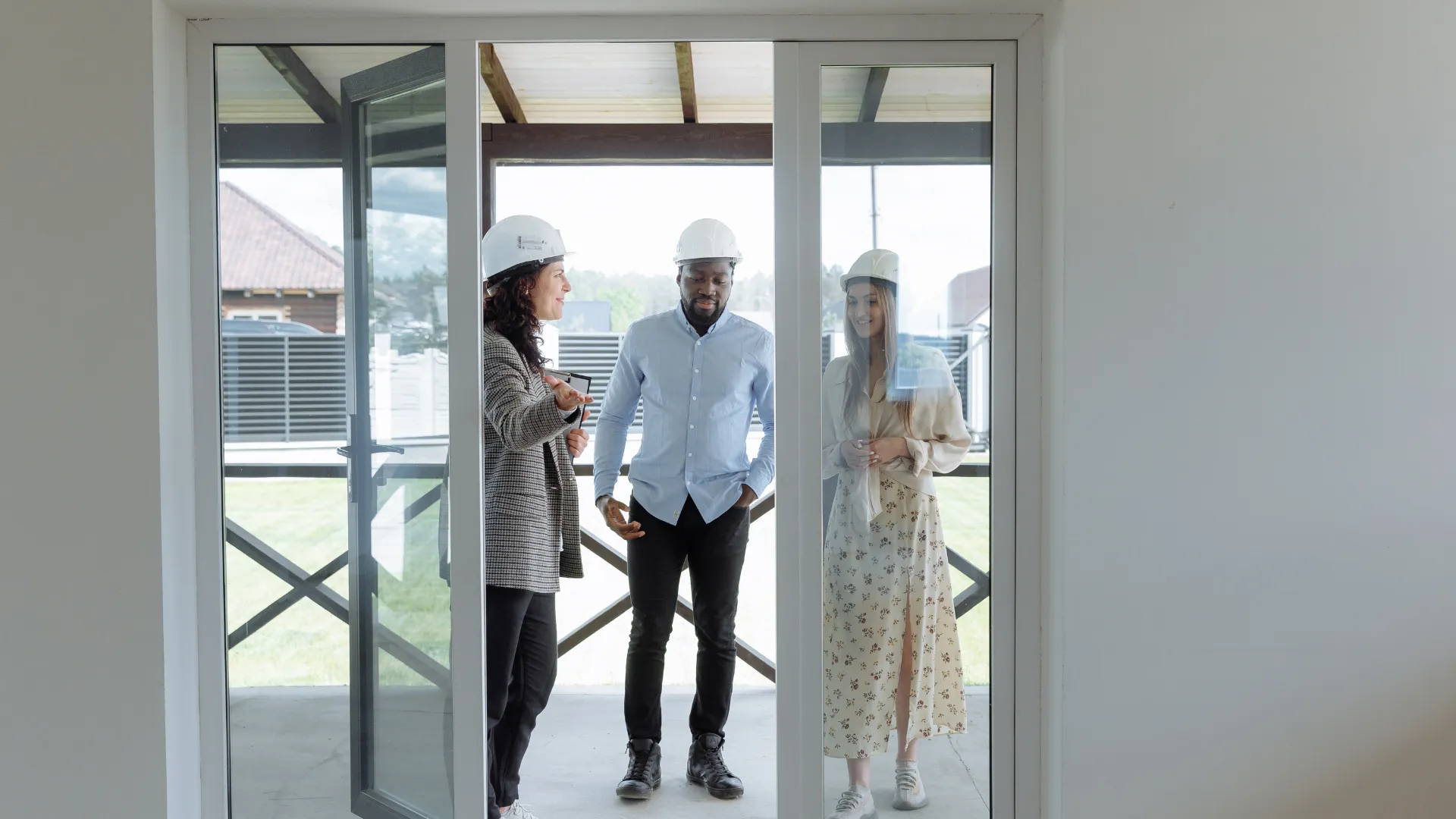 Contractor in a hard hat walking two clients through a new home