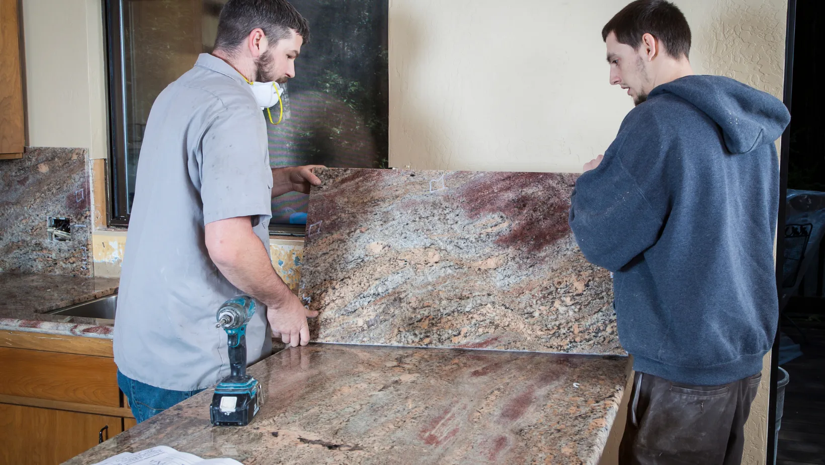 Two installers positioning a granite countertop slab in a kitchen.