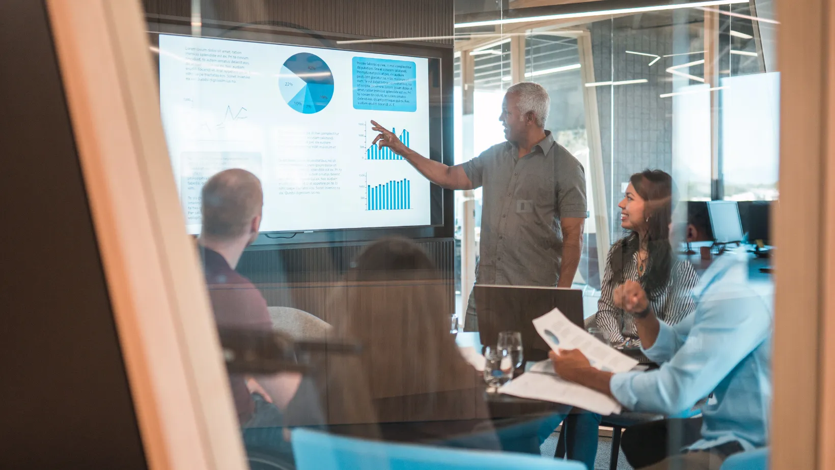 A presenter pointing at sales charts during an office meeting.