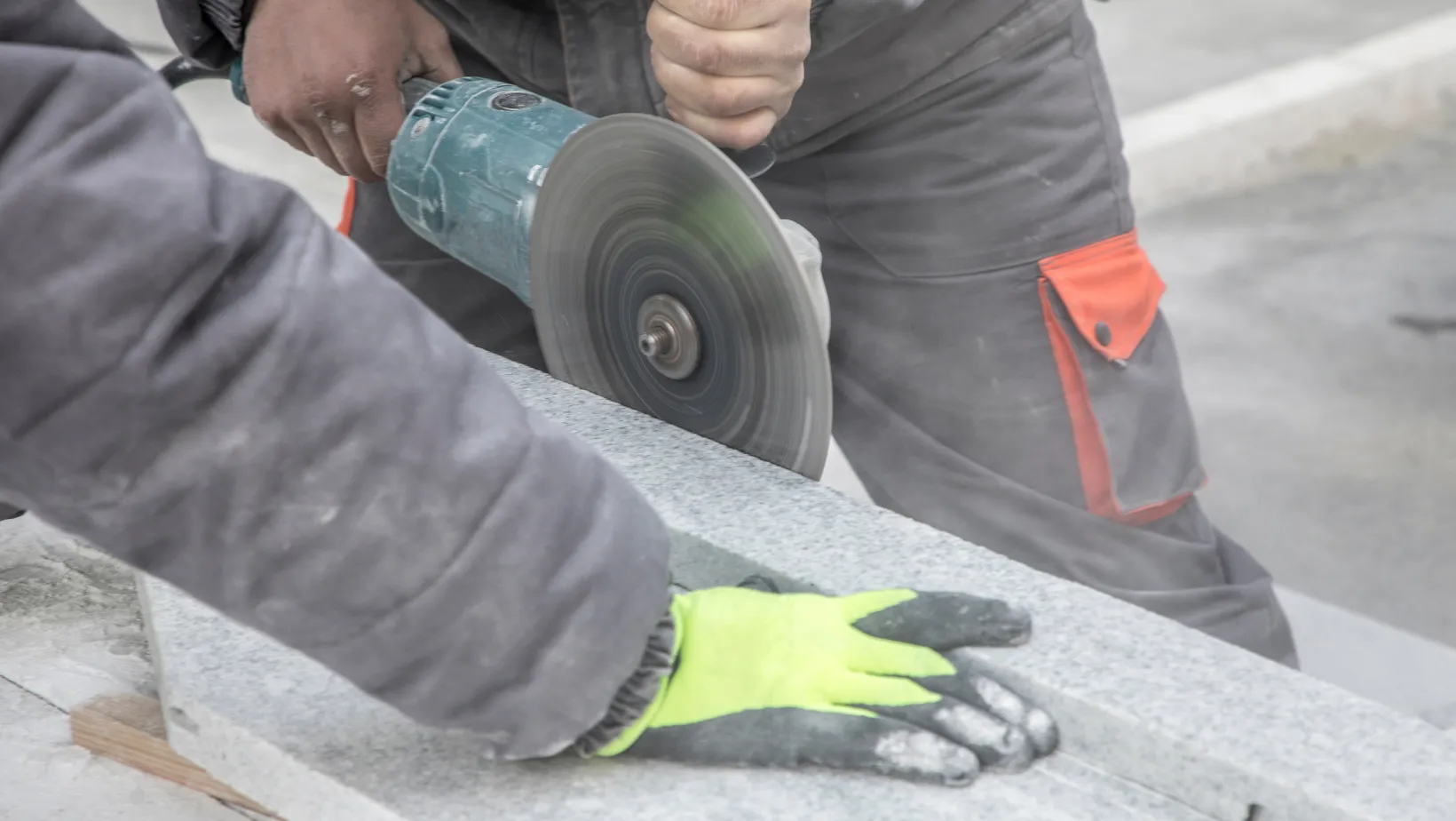 A gloved hand steadying a stone slab while it is cut.