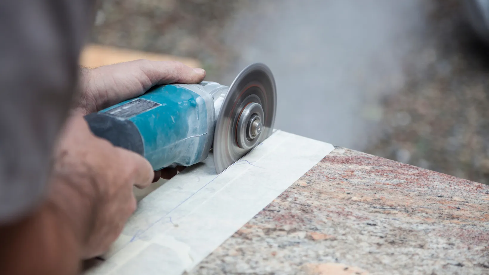 Hands cutting the edge of a granite countertop with a grinder.