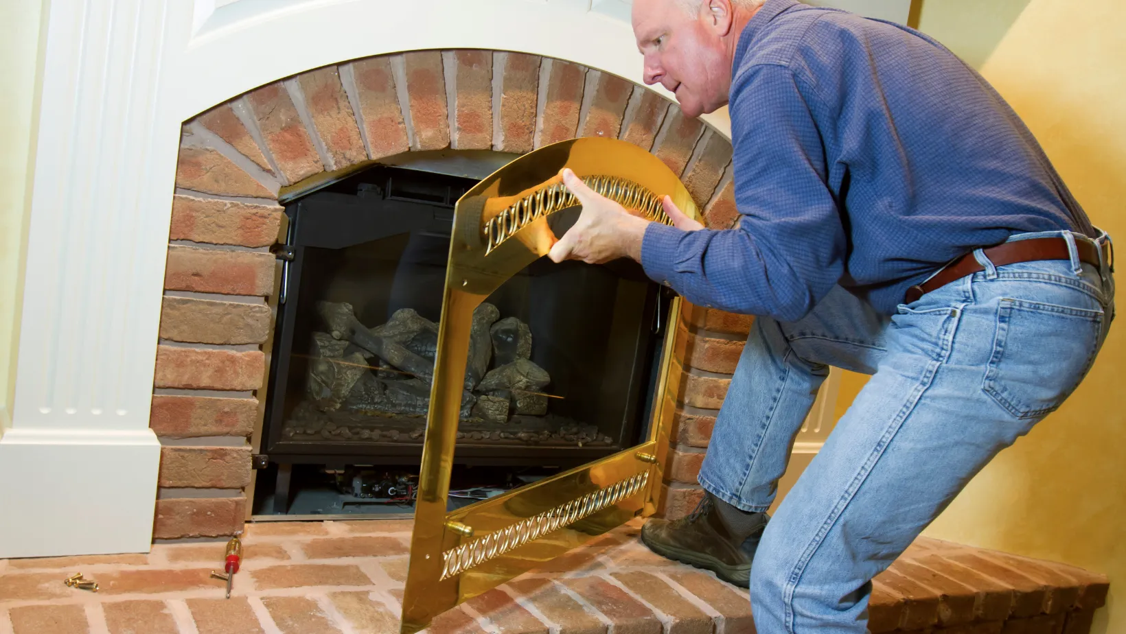 A technician fitting a brass screen on a brick fireplace