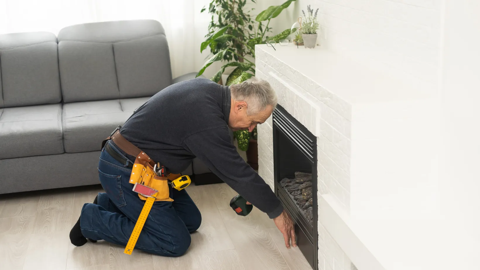 A technician kneeling beside a fireplace with a drill