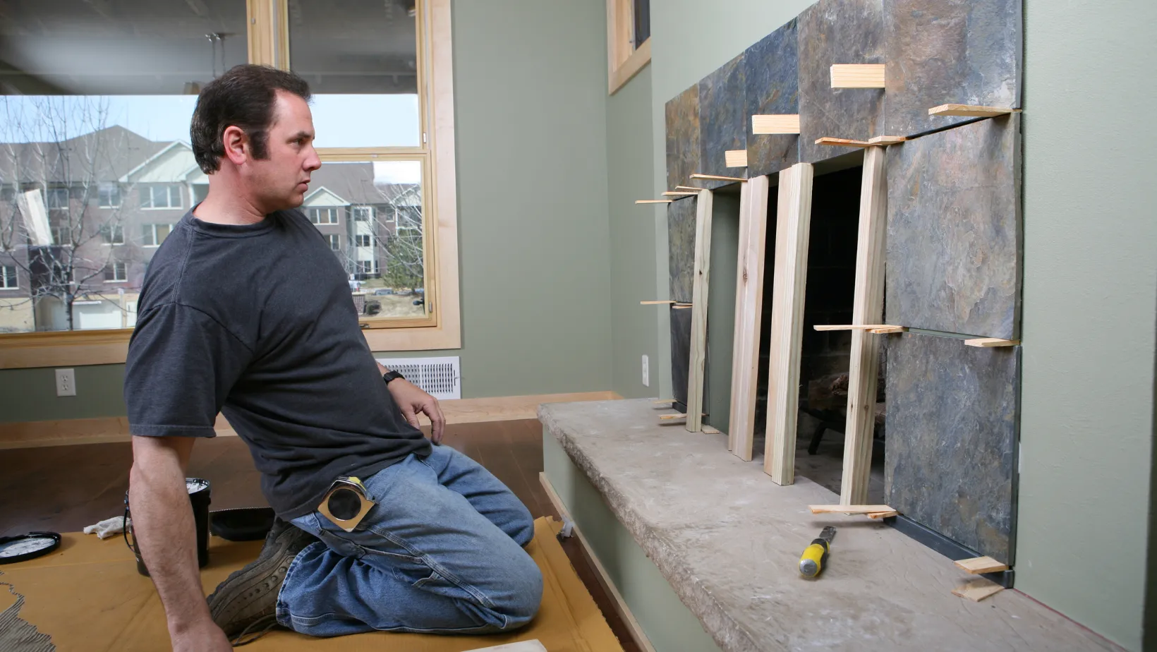 A contractor fitting stone tile around a fireplace opening