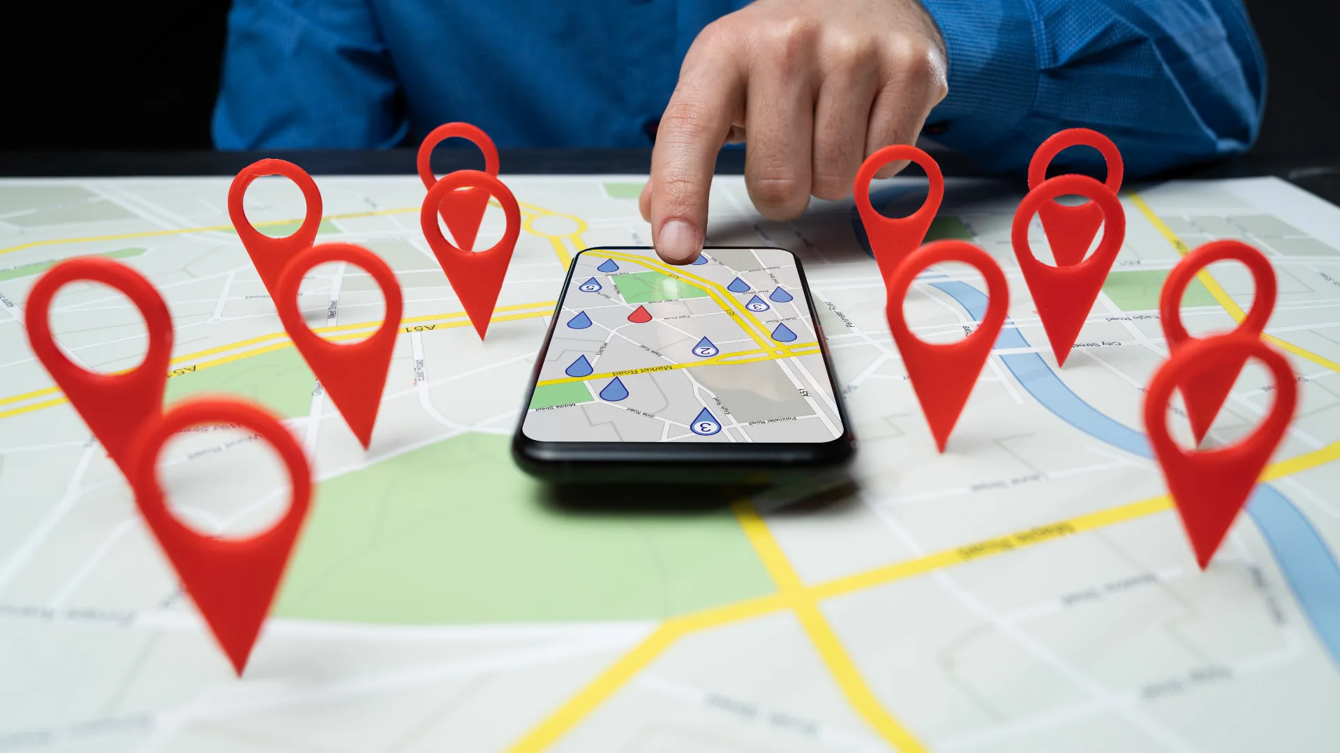 A hand taps a phone map surrounded by red location pins