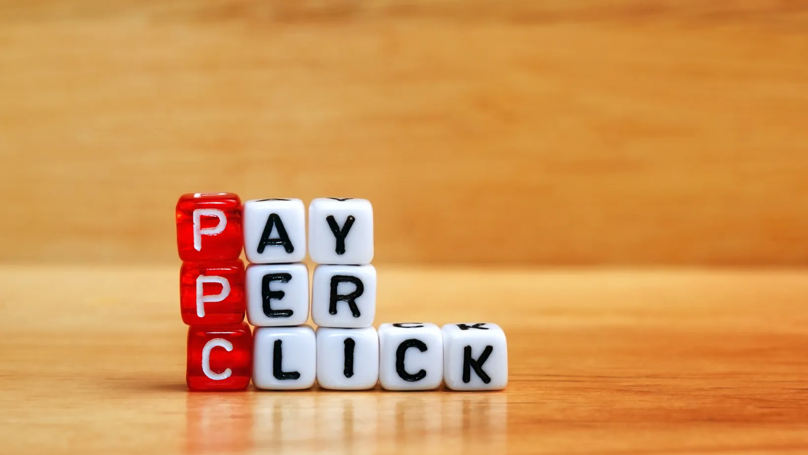 Red and white letter dice spelling Pay Per Click on a wooden table