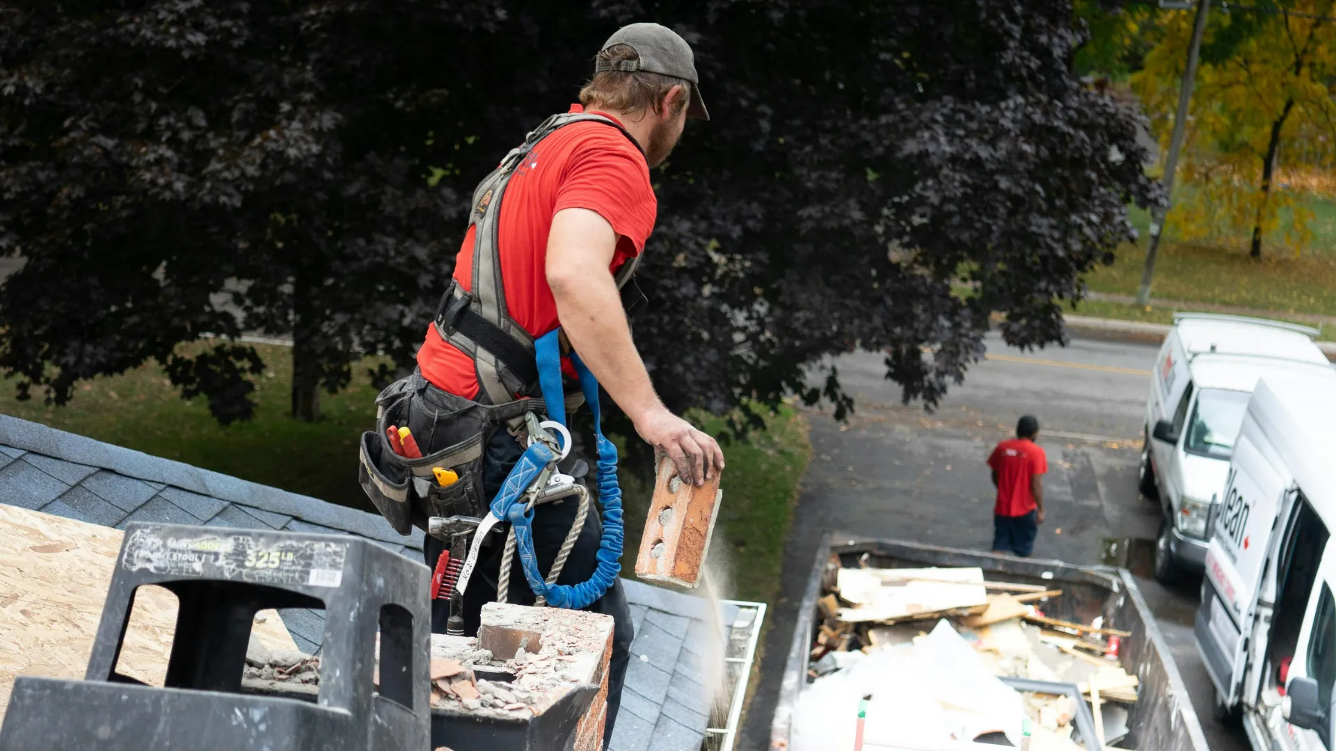 A roofer working on a chimney above a job site with service vans