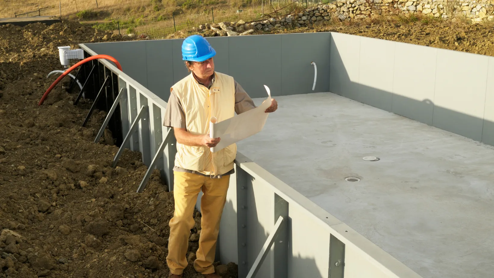 Pool builder reviewing plans beside a pool shell