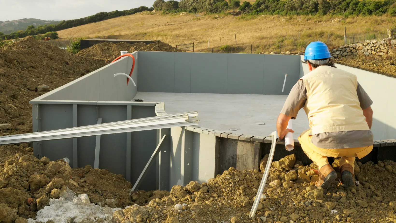 Builder kneeling beside a pool shell on a job site